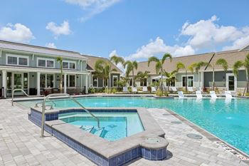 A swimming pool surrounded by a tiled patio and a building with a glass facade at The Junction at Rockledge Apartments, Rockledge, Florida